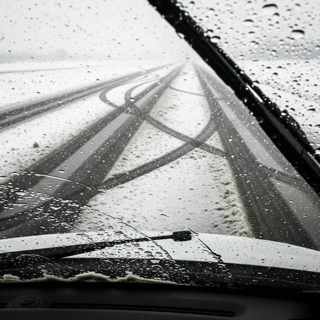 POV of panicking driver in a car during a slush storm, with smudged wipers and zigzagging tire tracks
